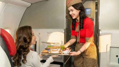A Vietjet flight attendant in red uniform serves a meal tray to a passenger