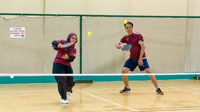 Two badminton players rally on an indoor court at Our Tampines Hub