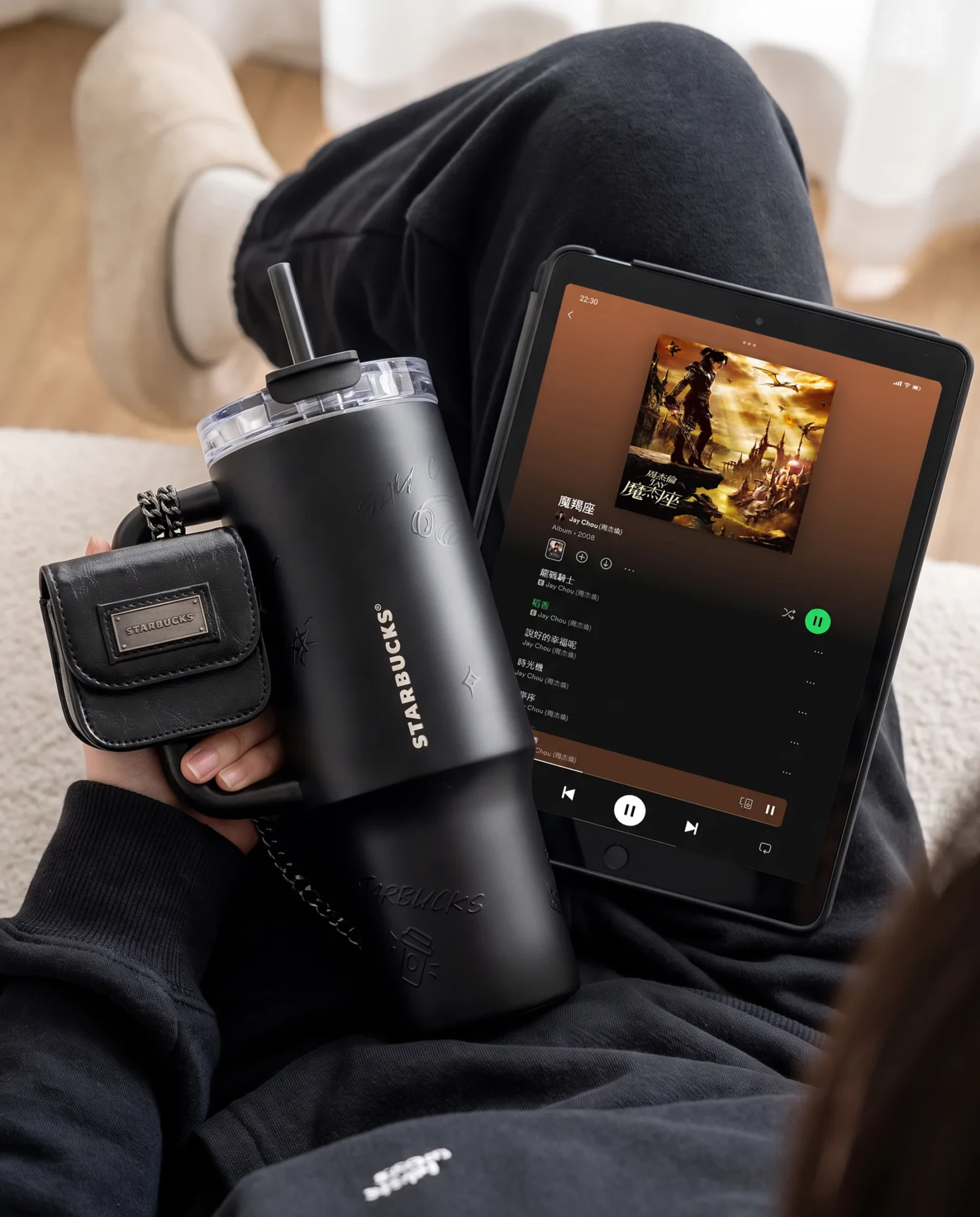 A person holding a Starbucks tumbler and card holder while using a tablet