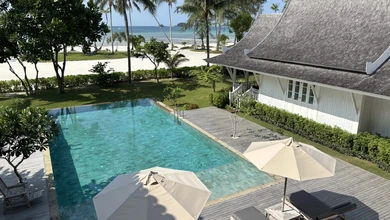 A beachfront villa at The Sanchaya with an infinity pool facing the ocean between palm trees