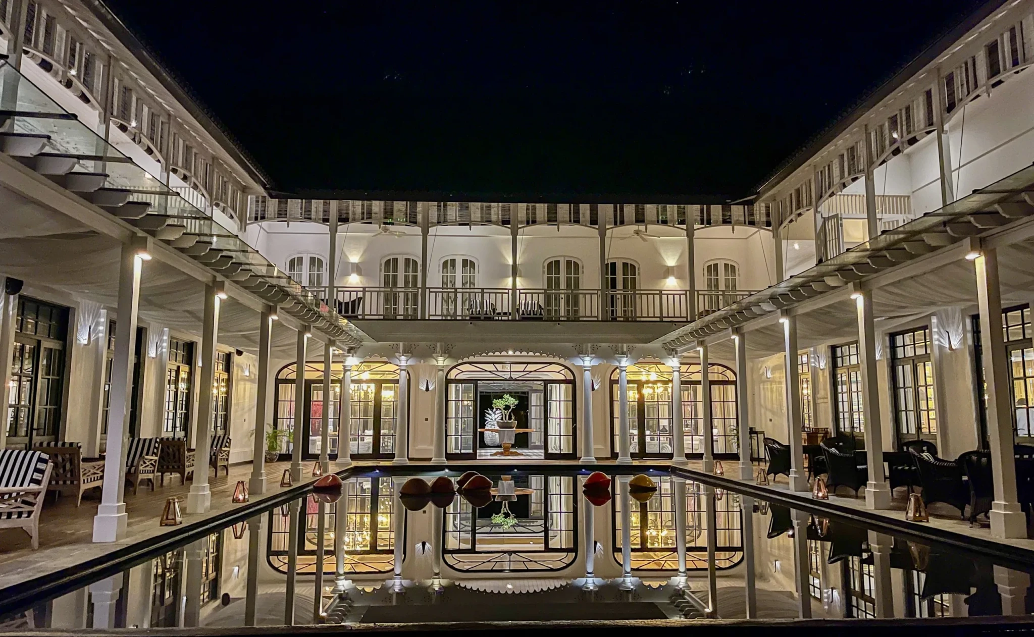 The Great House at The Sanchaya lit up at night, with white columns and arched windows around a courtyard