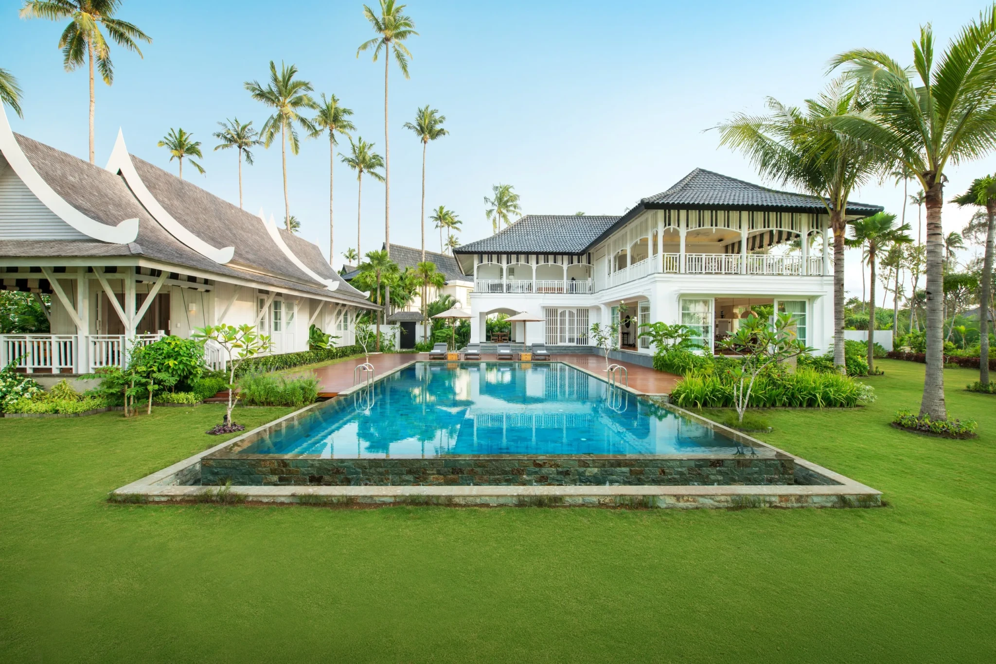 Vanda Villa's symmetrical white buildings around a rectangular pool with terracotta decking, lawns, and palms