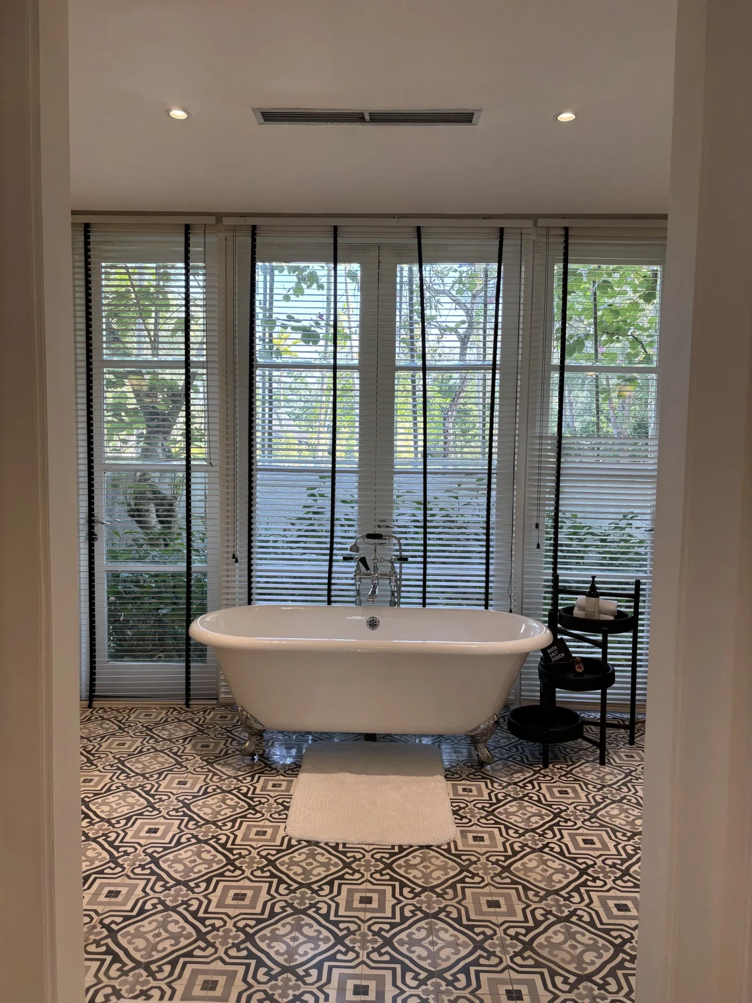 A white freestanding bathtub in front of large windows with black-framed glass doors and plantation shutters