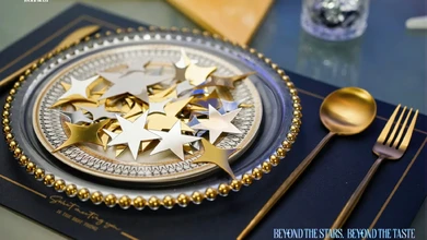 Trip.Gourmet fine dining table setting with a gold and white star-decorated plate, gold flatware and a dark blue placemat