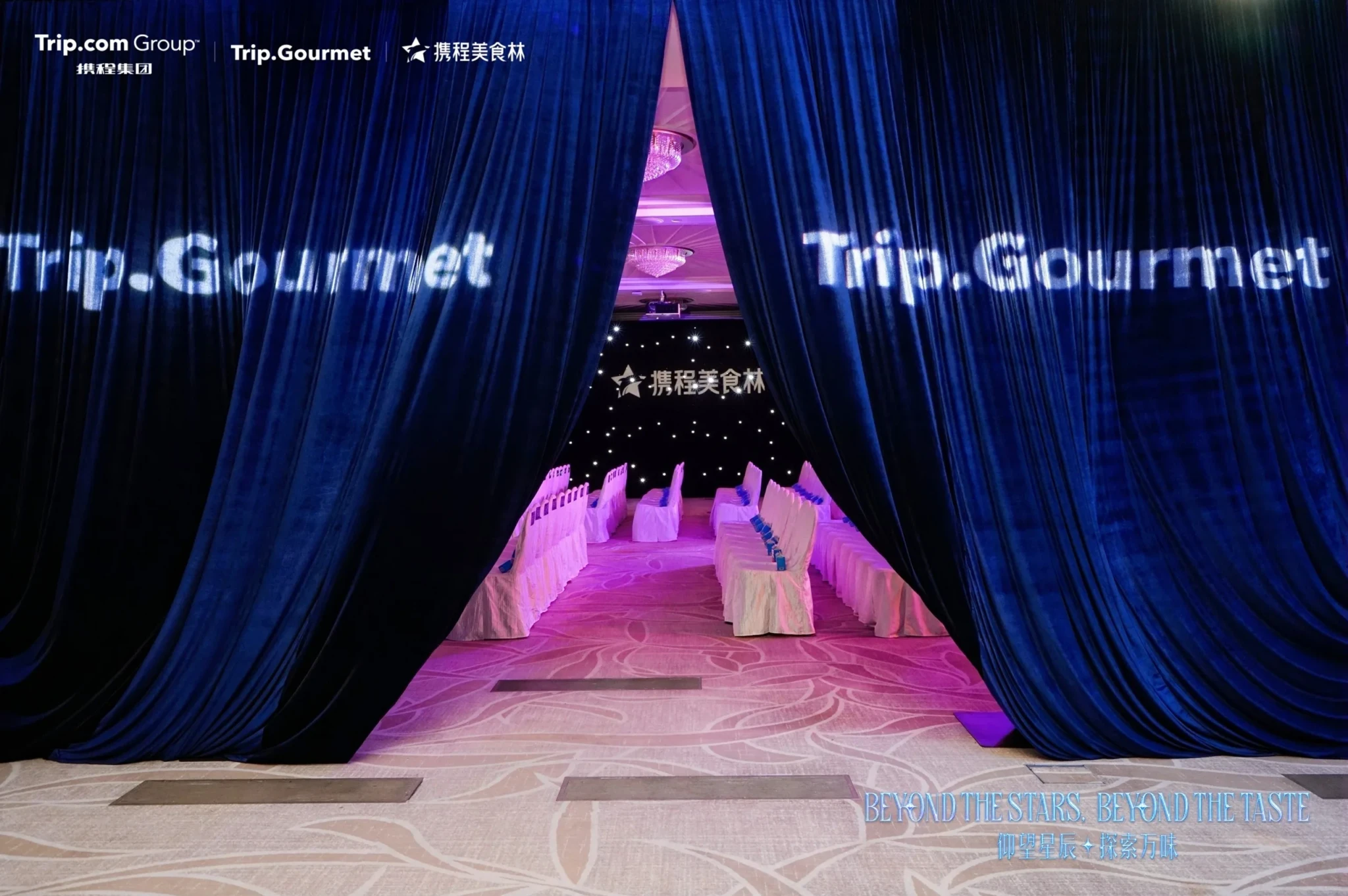 Trip.Gourmet event venue entrance framed by blue velvet curtains with a pink-lit dining space beyond