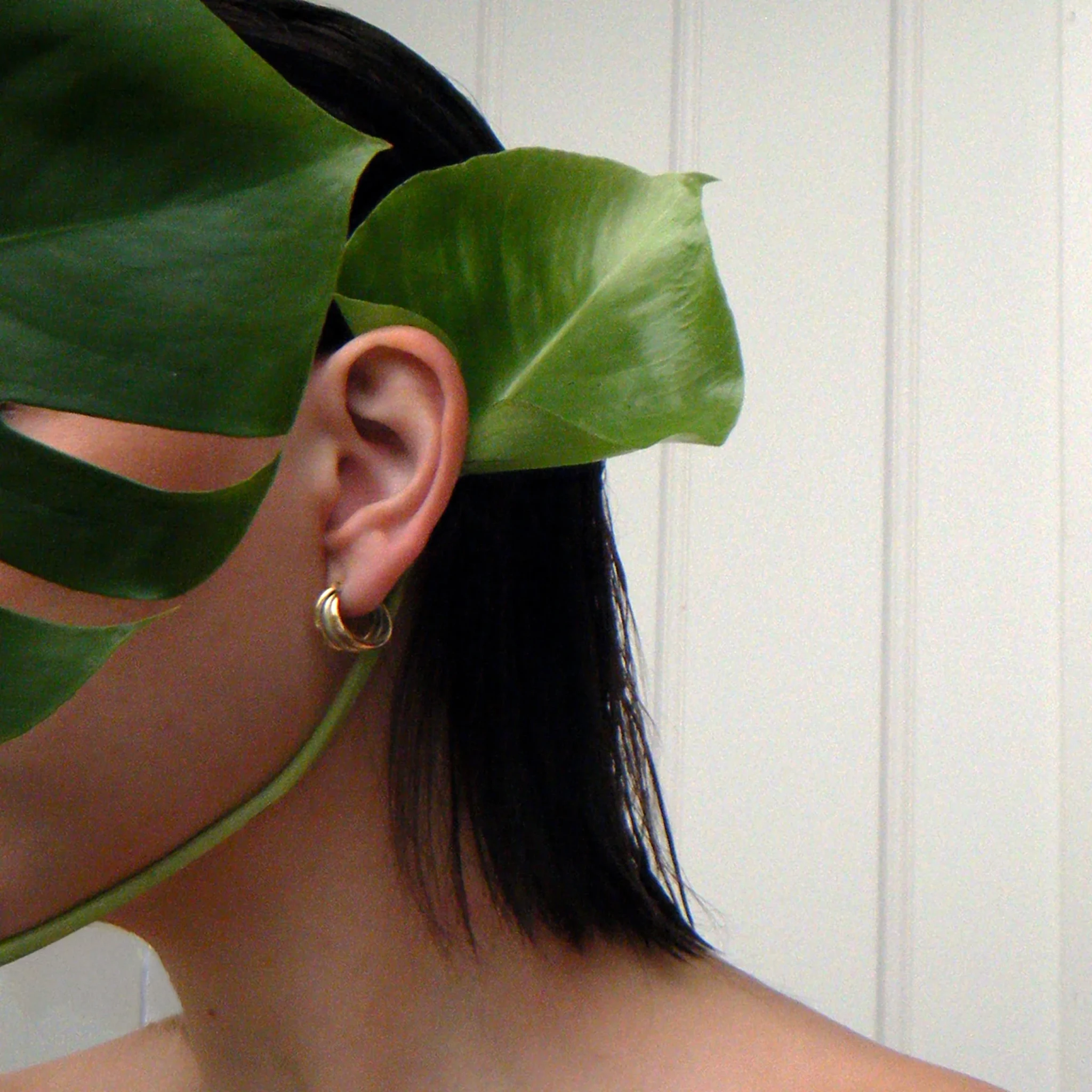 Surreal artwork where oversized green leaves replace a person's head against a plain white interior