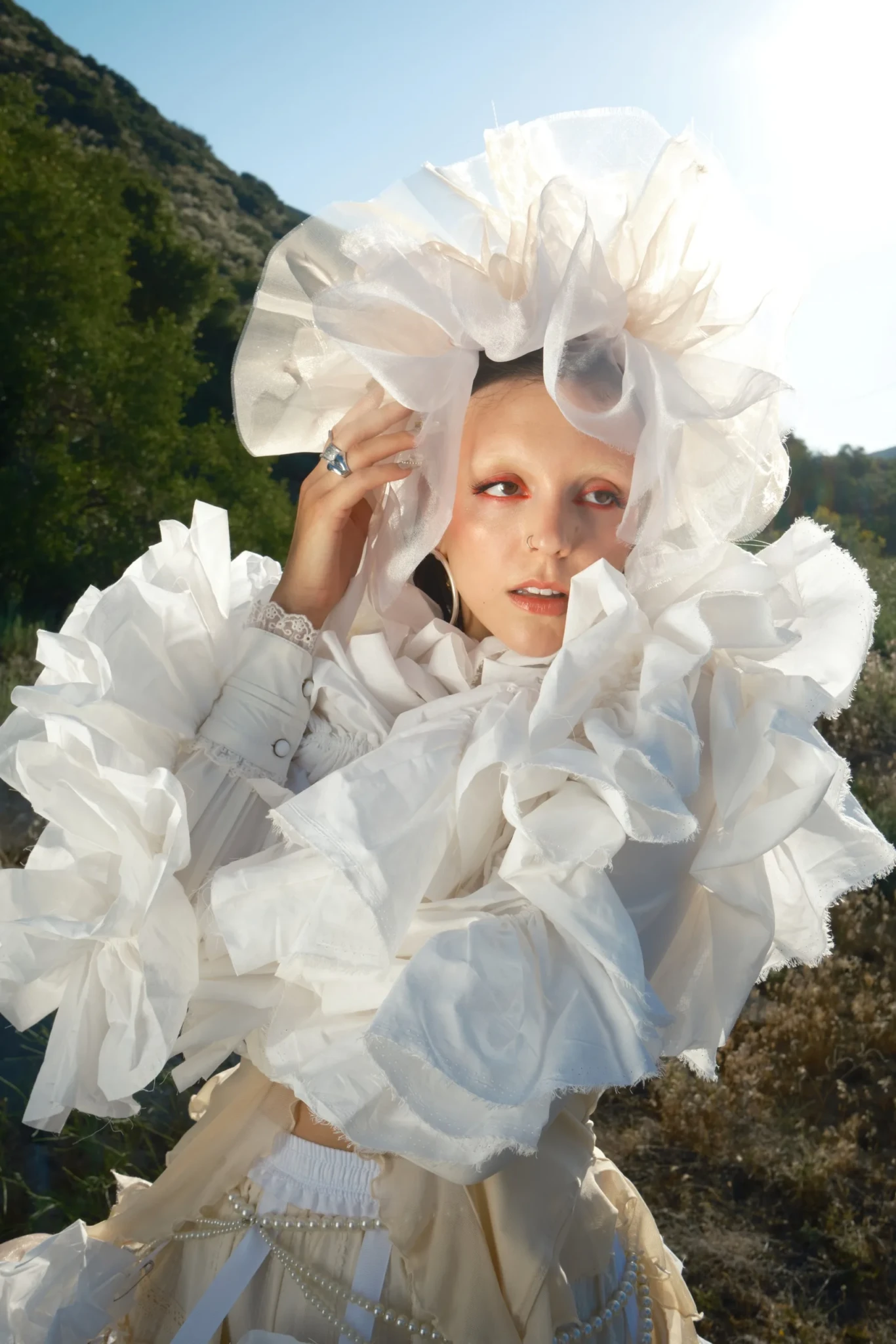 googly eyes on a green hillside in an elaborate white costume with an oversized eye-shaped headpiece