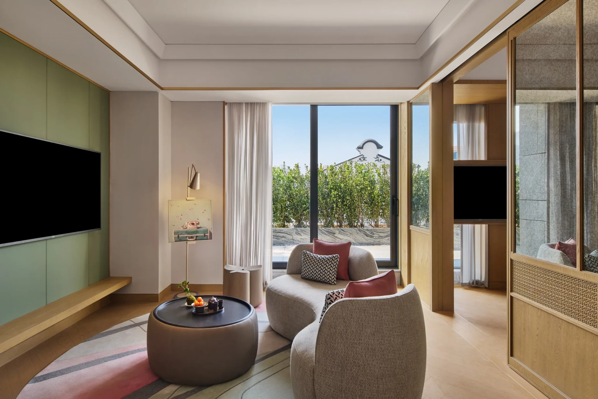 Guest room living area with curved upholstered seating and floor-to-ceiling windows onto a planted terrace