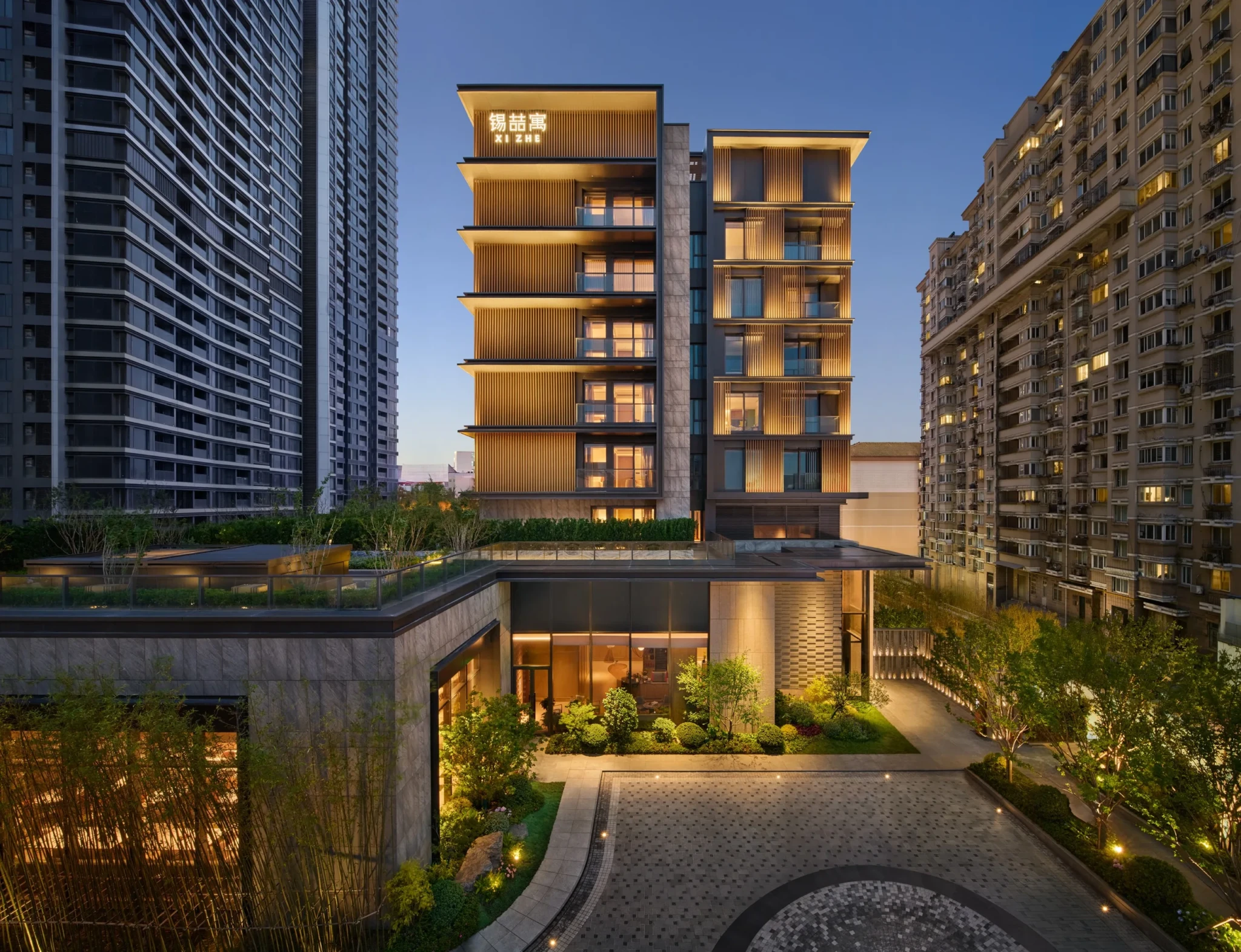 Xi Zhe Wuxi's wood-slat facade lit at dusk among the older apartment blocks around it