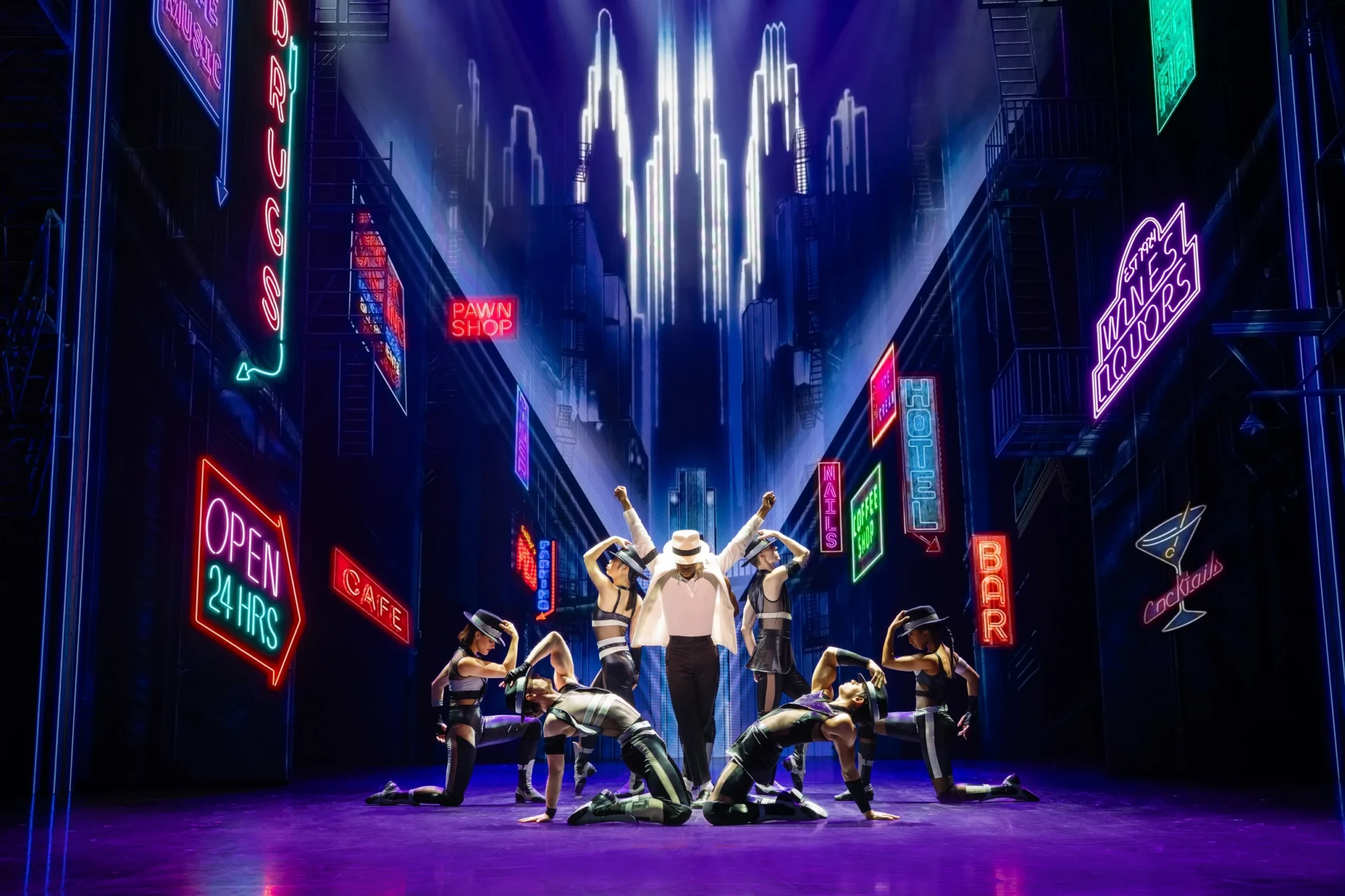 The lead performer and ensemble of MJ The Michael Jackson Musical posing against a neon-lit cityscape set