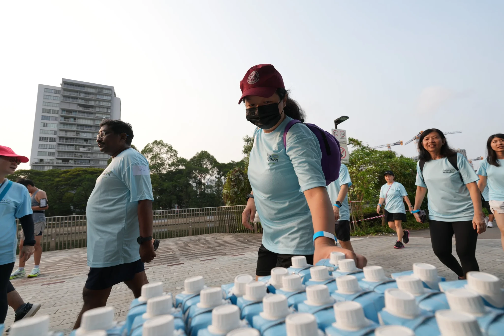 Galaxy Walkathon participants in light blue shirts walk past refreshment stations at The Kallang