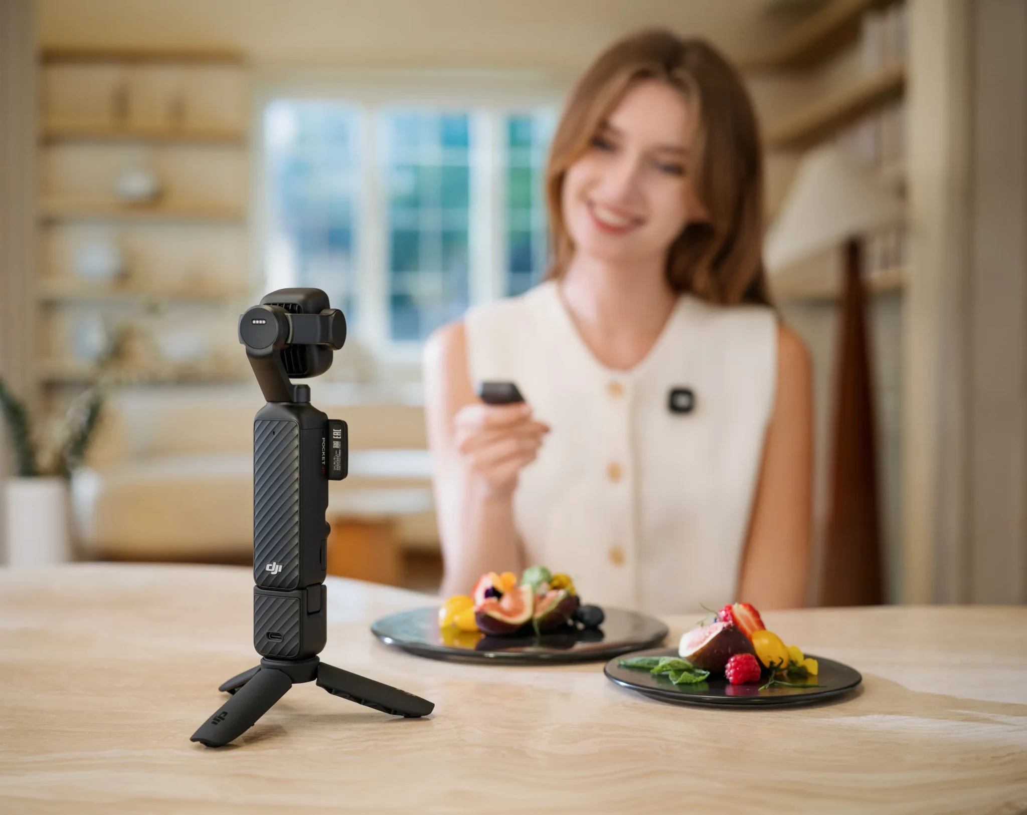 The DJI Osmo Pocket 4P on a tripod filming a dining scene with dessert plates and a woman in the background