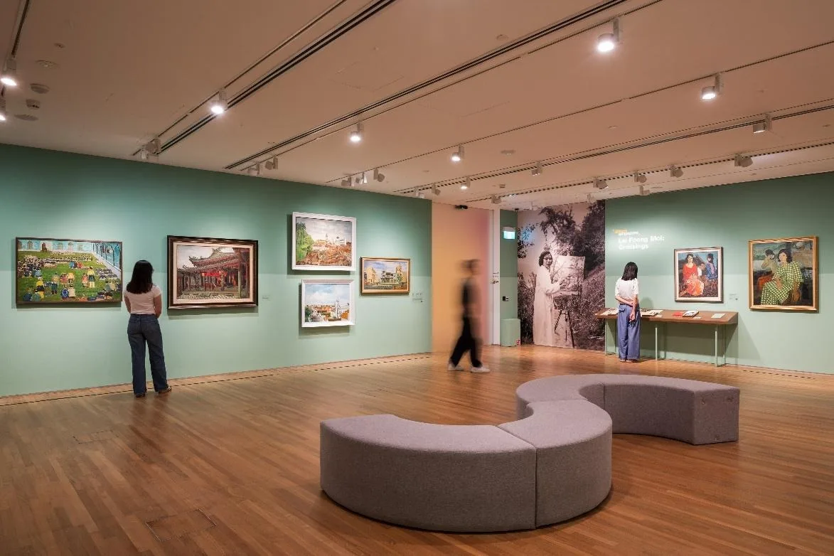 Paintings on green gallery walls around a curved grey bench, with a large photo panel reading Lai Foong Moi: Crossings