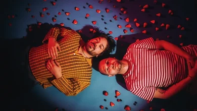 Milky Chance posing symmetrically against a blue background with red heart-shaped confetti