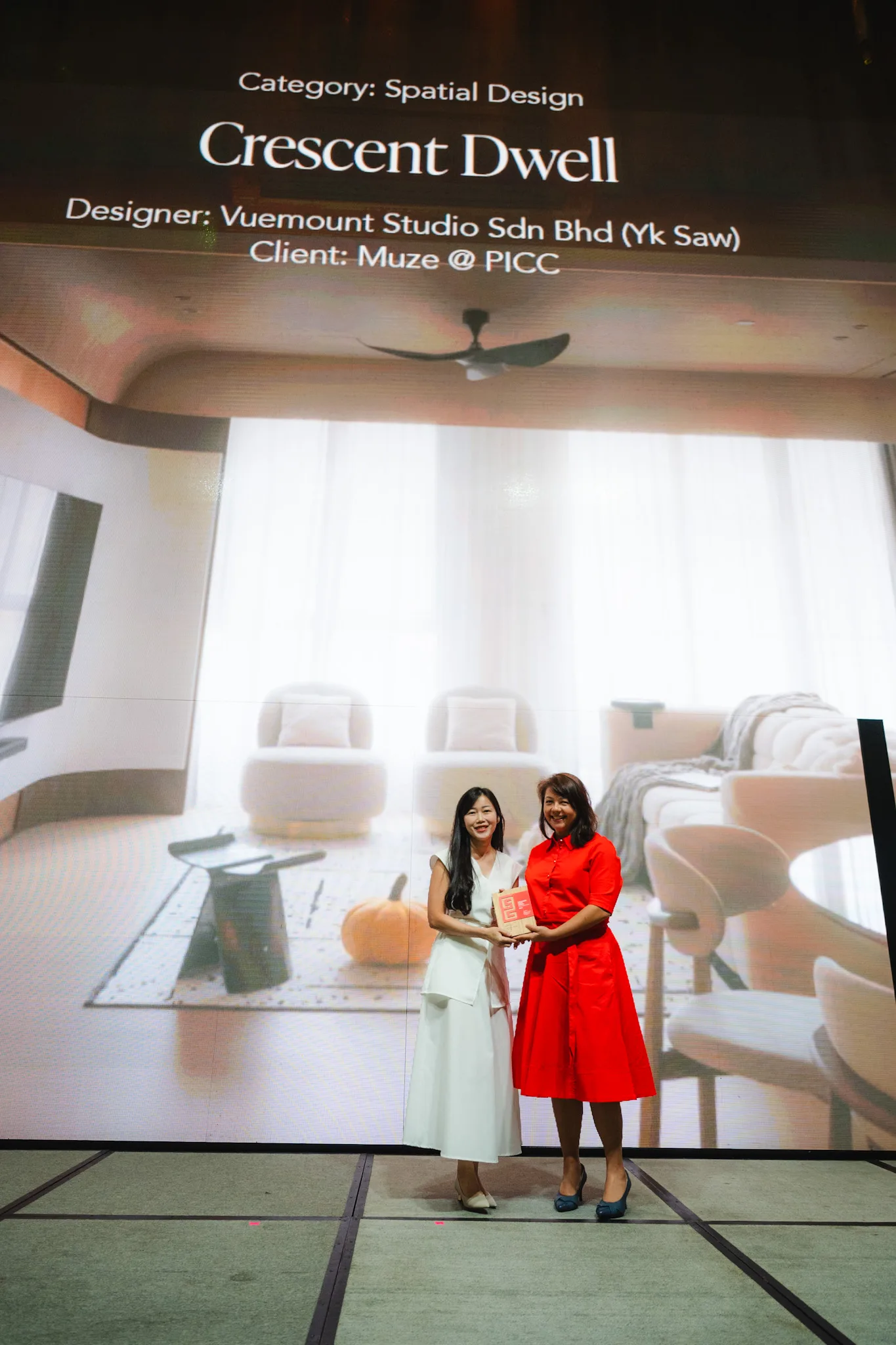 Two women present the Crescent Dwell residential interior on a large screen