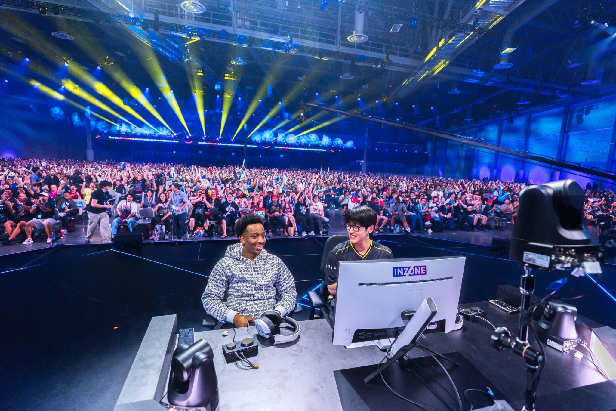 Broadcast commentators at an Evo event with a large crowd of spectators behind them