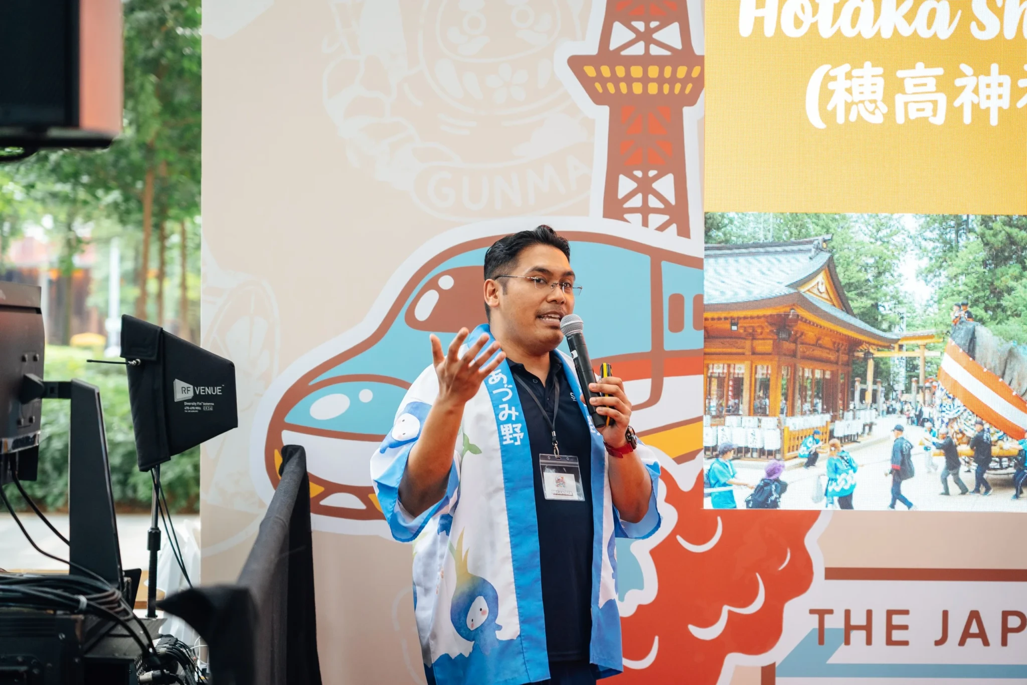 A speaker in traditional Japanese festival attire presenting on stage at The Japan Rail Fair