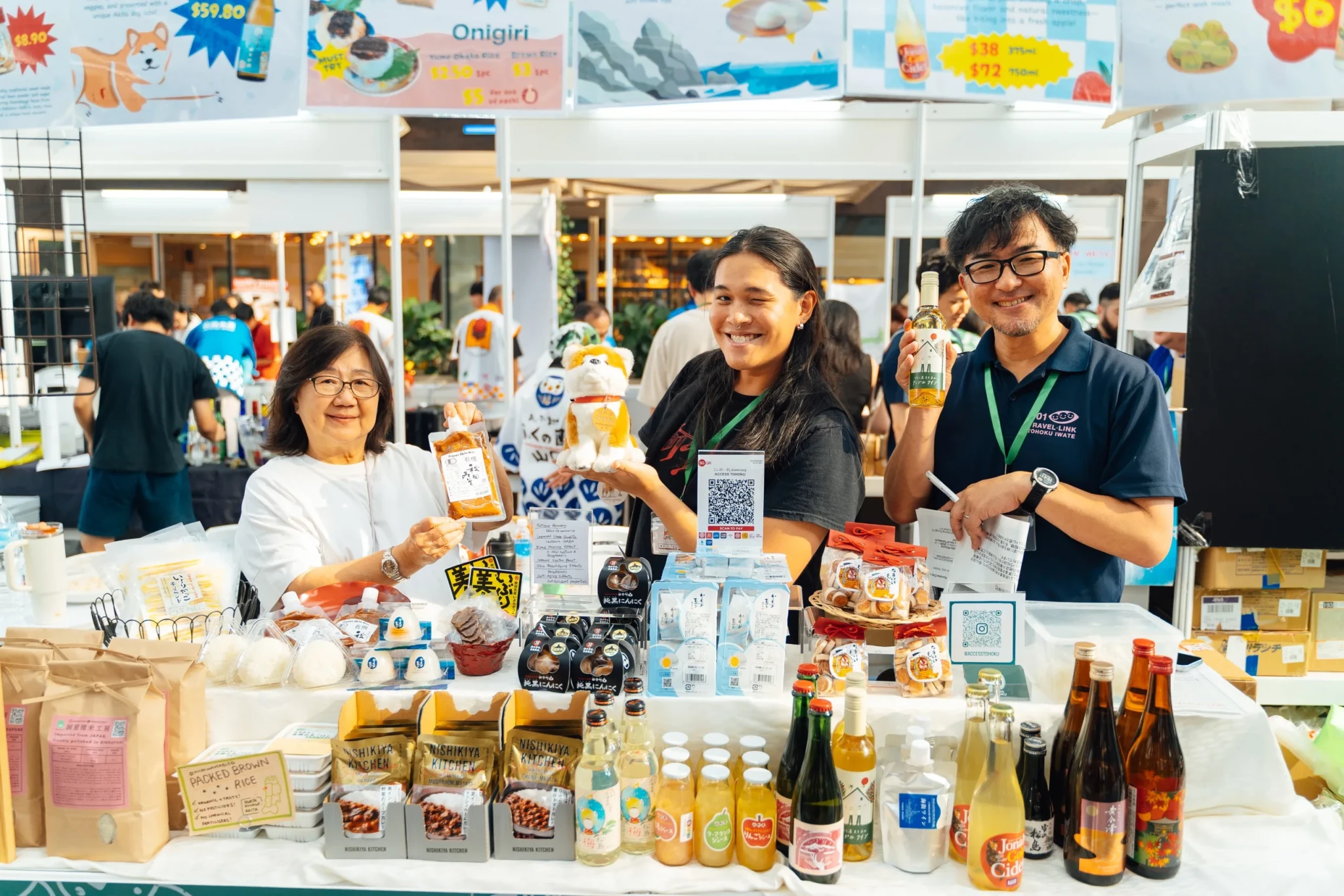 Staff at the Access Tohoku booth displaying regional Japanese sake, beer and packaged snacks