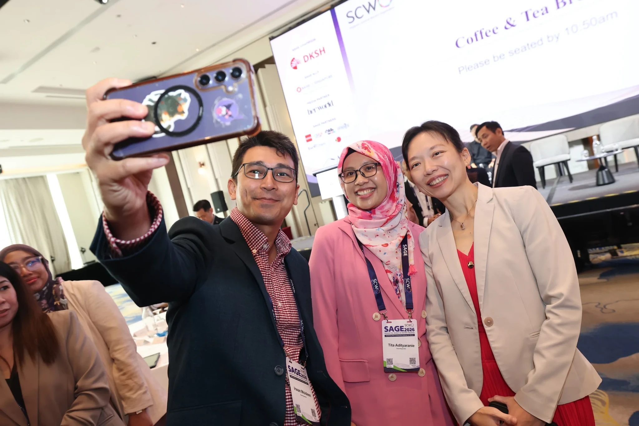 Group of SAGE2026 conference attendees taking selfie with smartphone macro lens