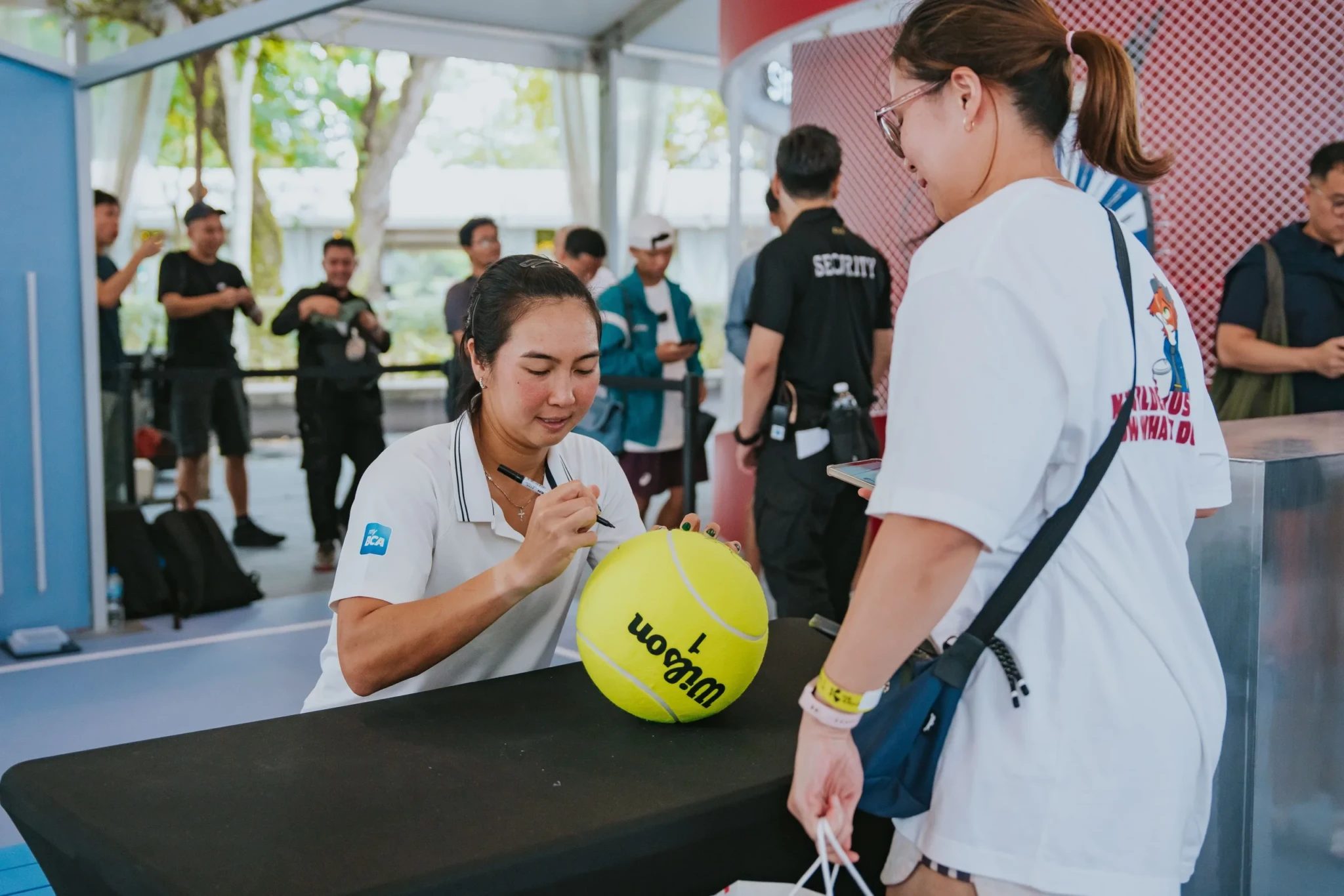A player signs a tennis ball for a fan at the Singapore Tennis Open players meet and greet
