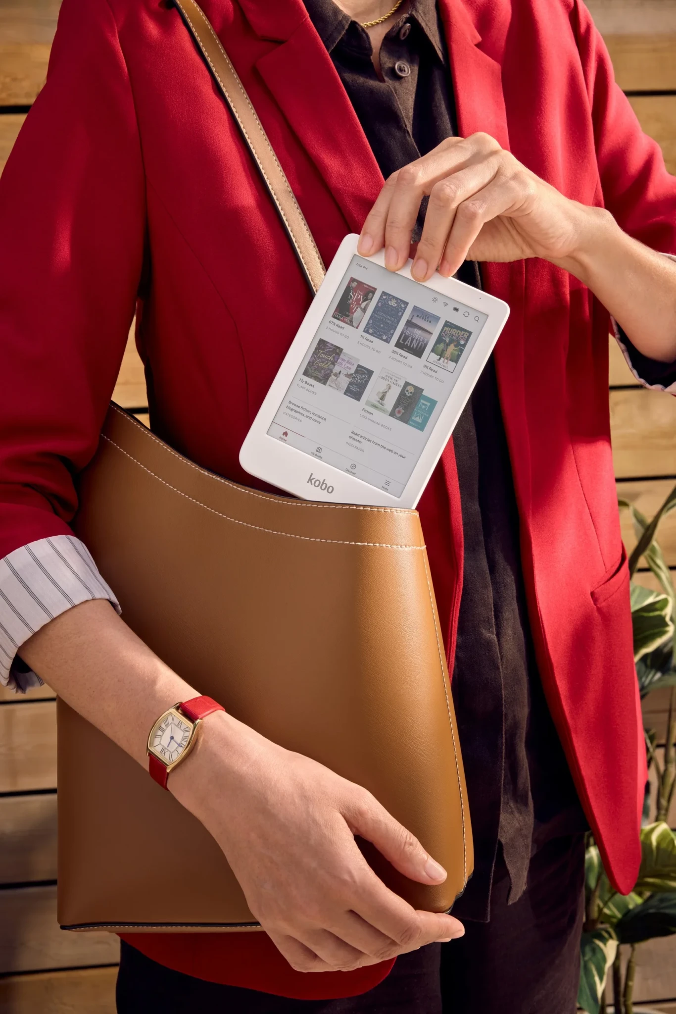 A person wearing a red jacket holds the white Kobo Clara Colour eReader, displaying its library browsing interface