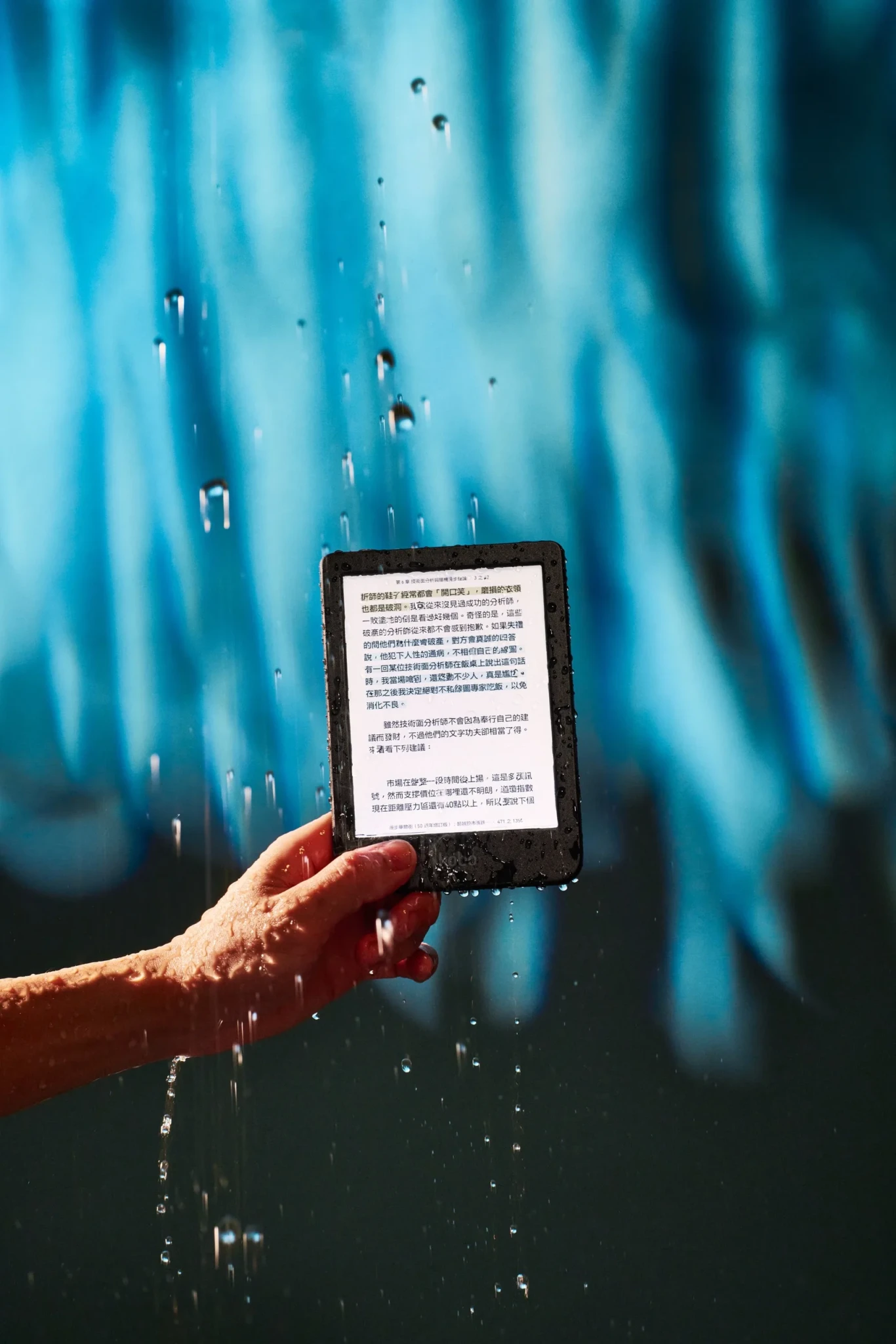 A hand holds a Kobo eReader displaying text in the rain