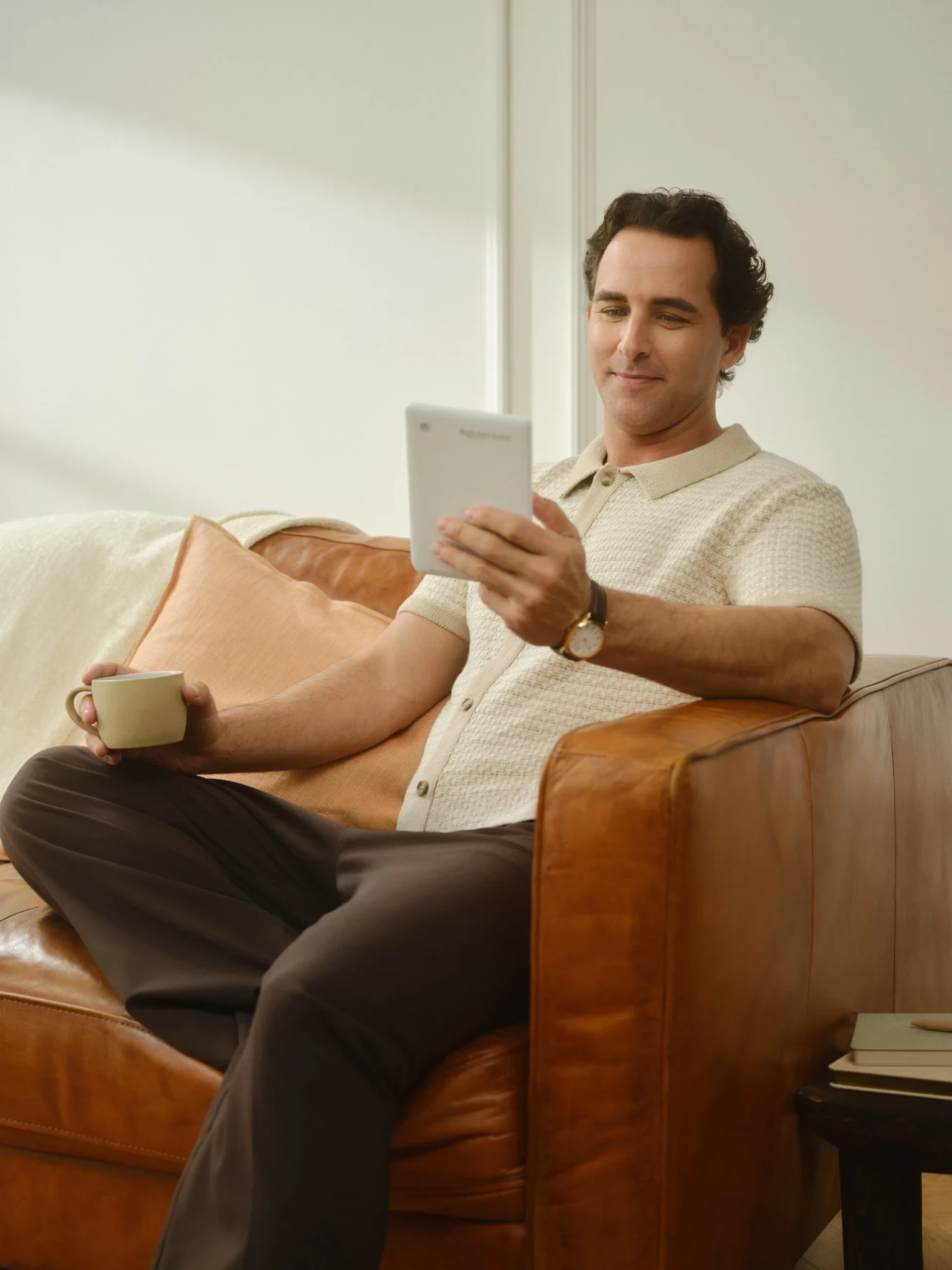 A man relaxes on a leather chair while reading on the Kobo Clara Colour eReader, holding a beverage