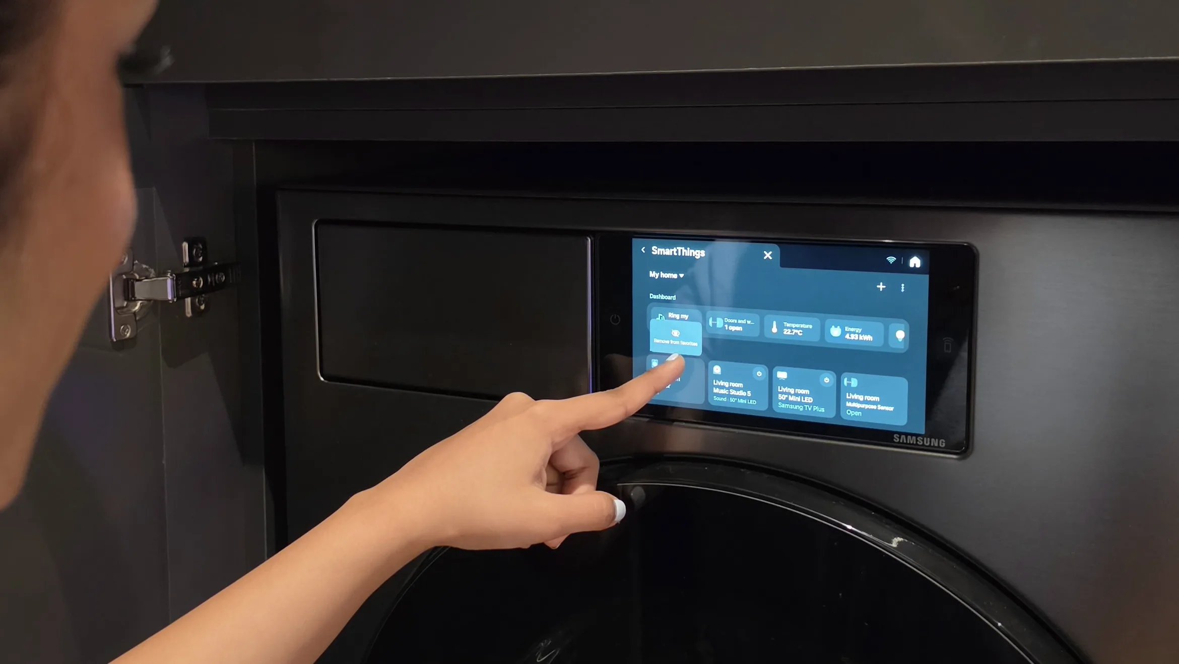 A hand reaching towards the SmartThings interface on a Samsung control panel