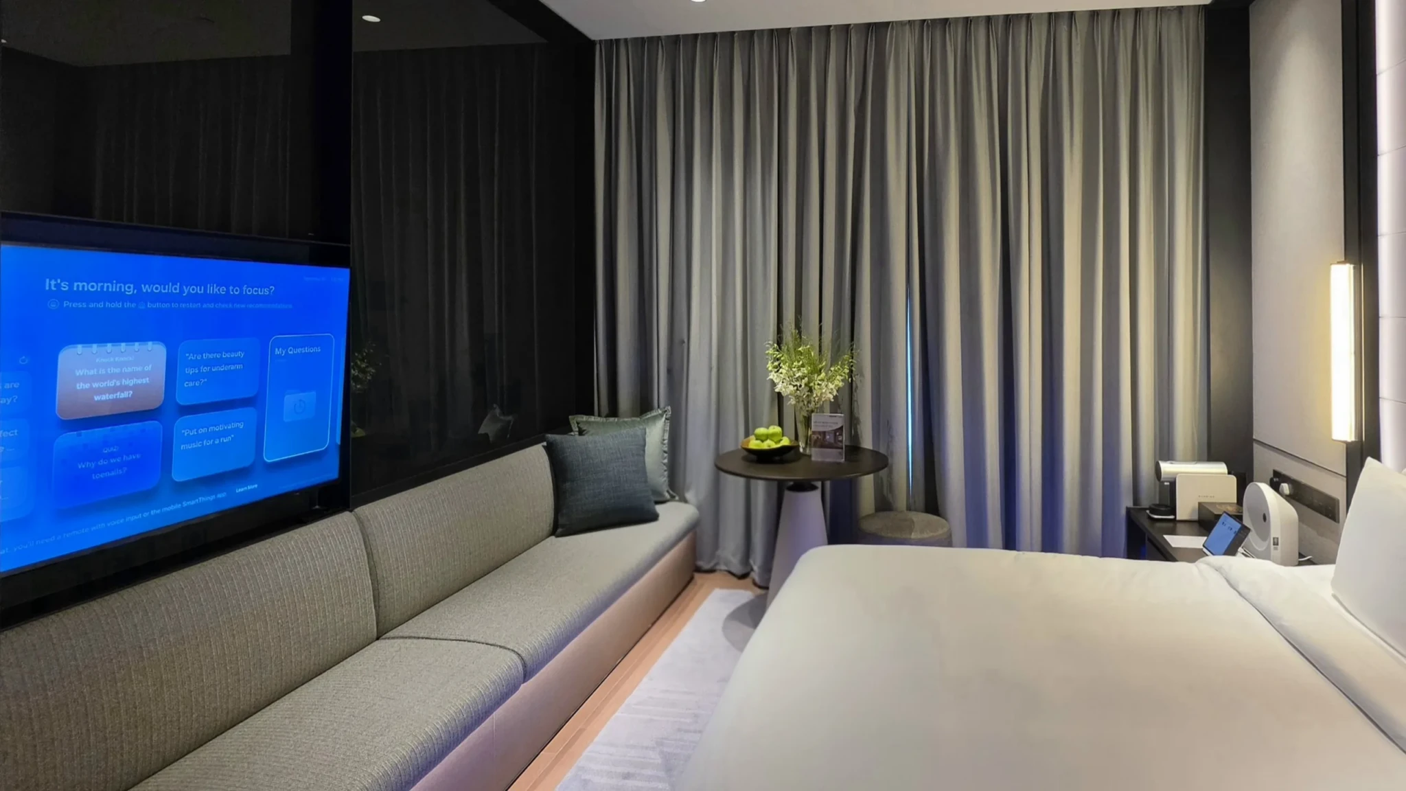 Hotel bedroom with a large TV displaying a blue SmartThings interface asking if the guest would like to focus this morning