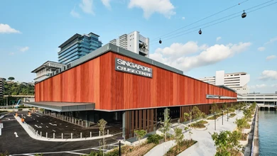 The new Singapore Cruise Centre HarbourFront terminal, clad in orange corrugated metal, seen from the waterfront with cable cars overhead