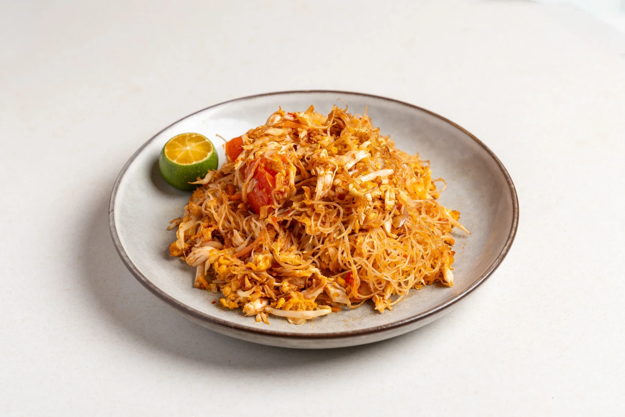 Sambal chicken fried bee hoon on a gray ceramic plate with lime garnish