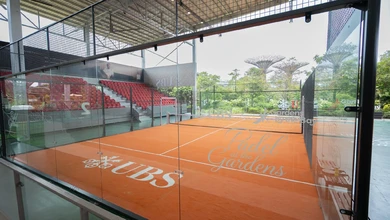 A UBS-branded padel court at Gardens by the Bay with the Supertrees rising behind the glass enclosure