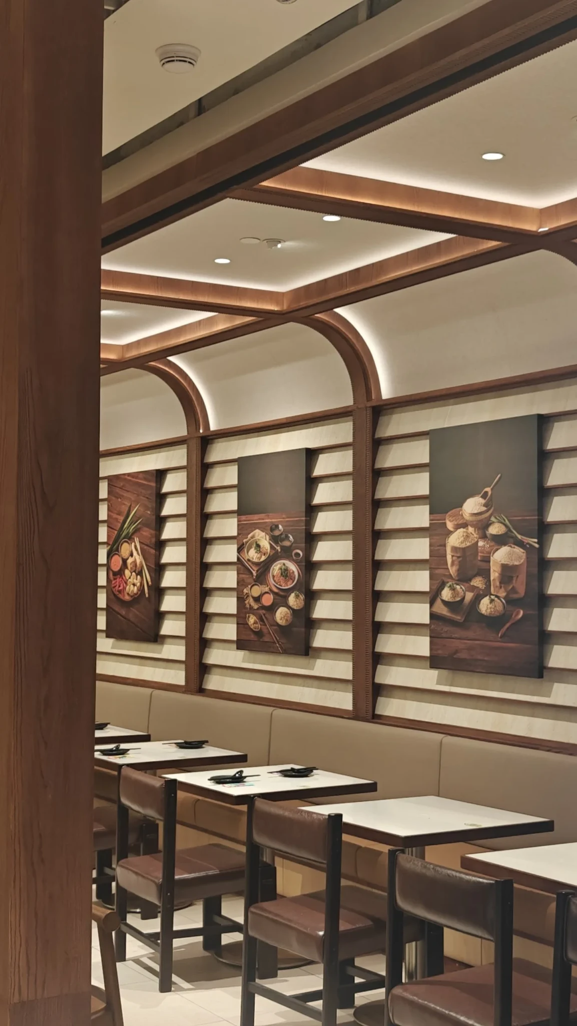 Modern restaurant interior with wood-framed architecture, dining tables, and food artwork panels