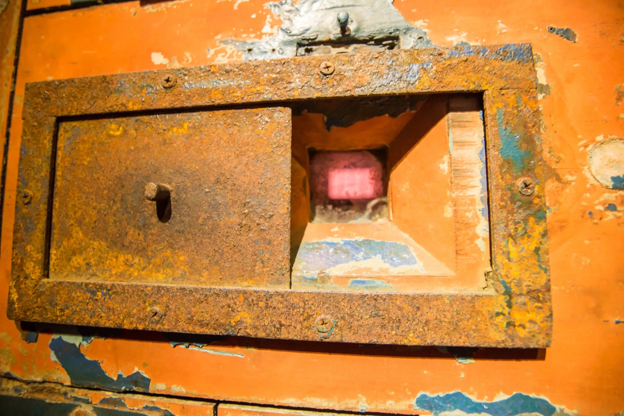 Weathered rusted metal frame with recessed compartment containing a red glowing indicator light