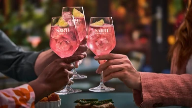 Two Sarti Spritz cocktails garnished with lemon wheels being toasted at a gathering
