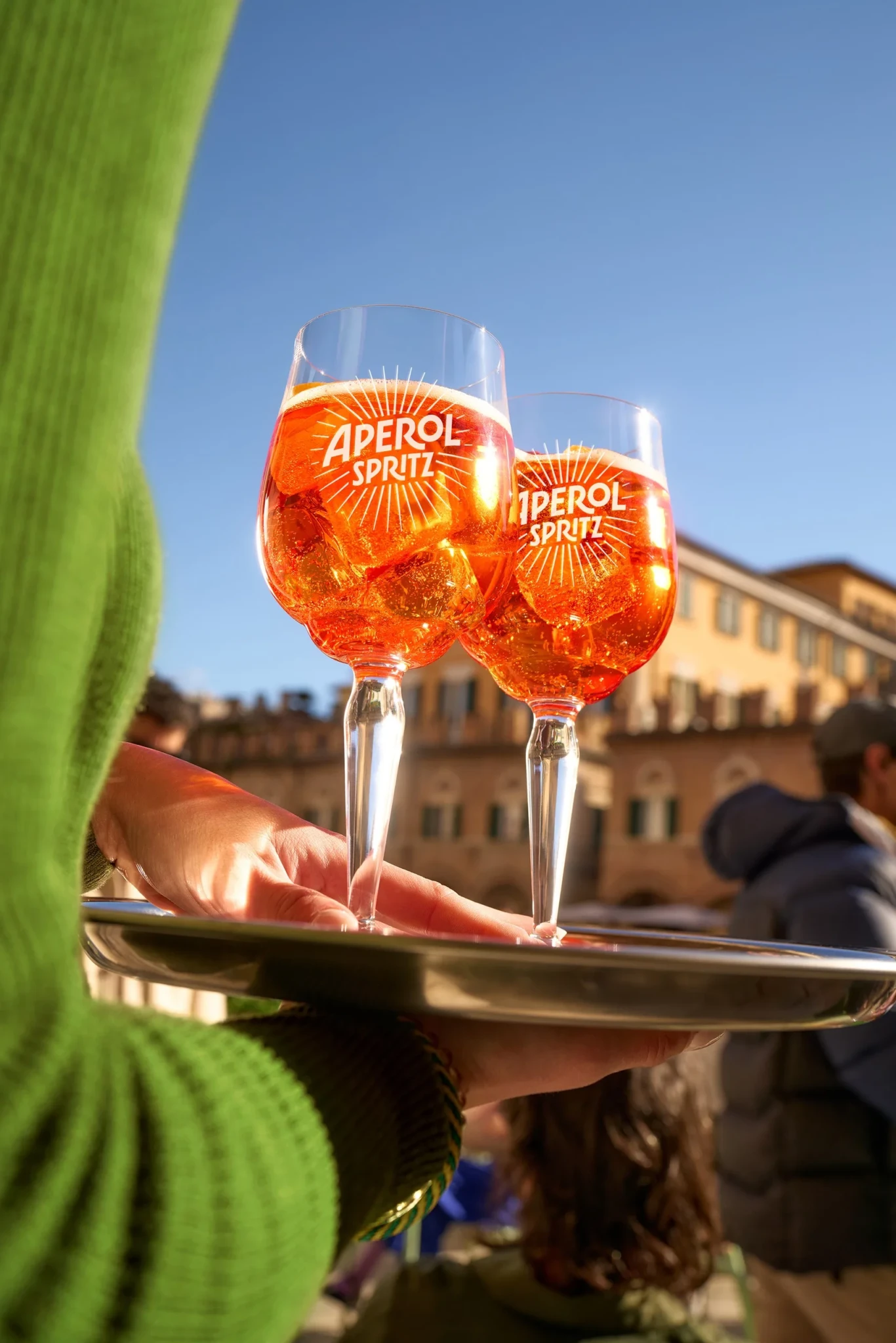 Two Aperol Spritz cocktails on a silver tray in bright daylight