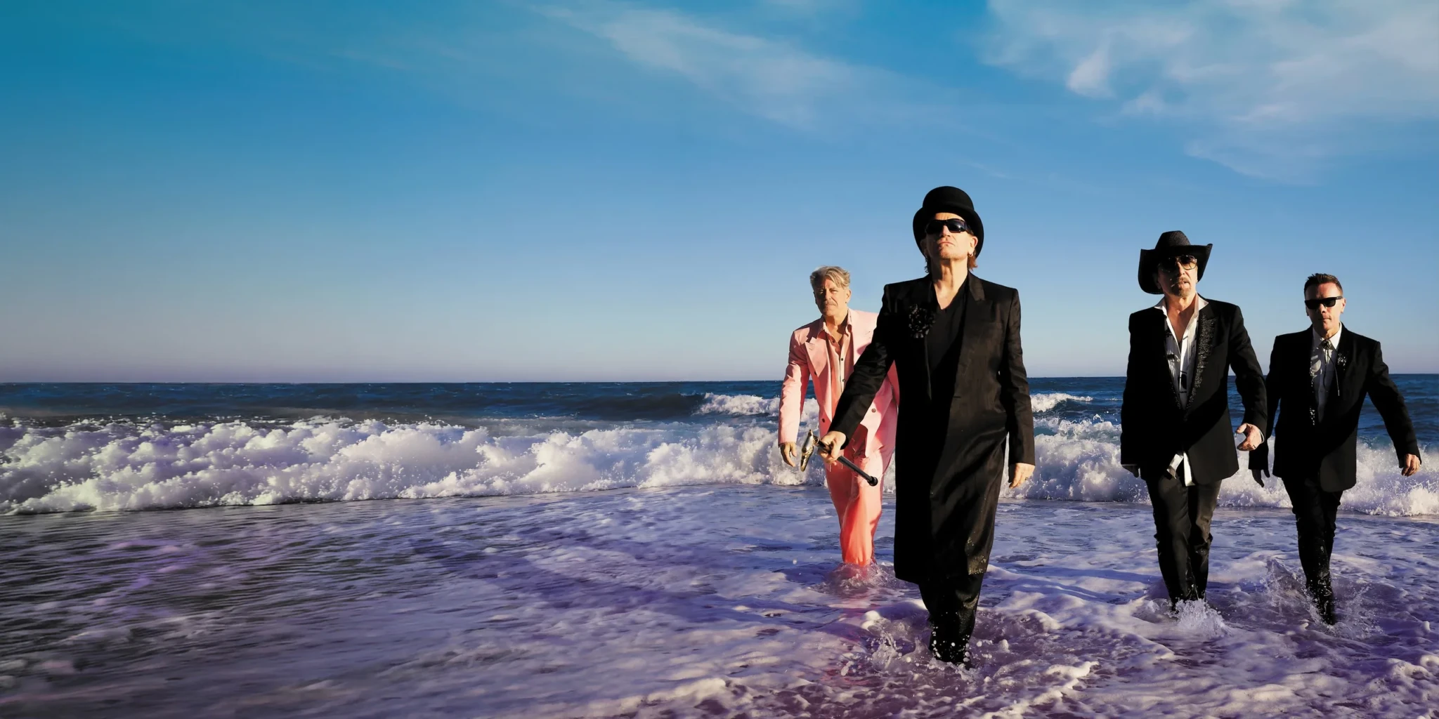 U2 in dark suits and hats wading into the ocean for the Carnaval De Luz shoot