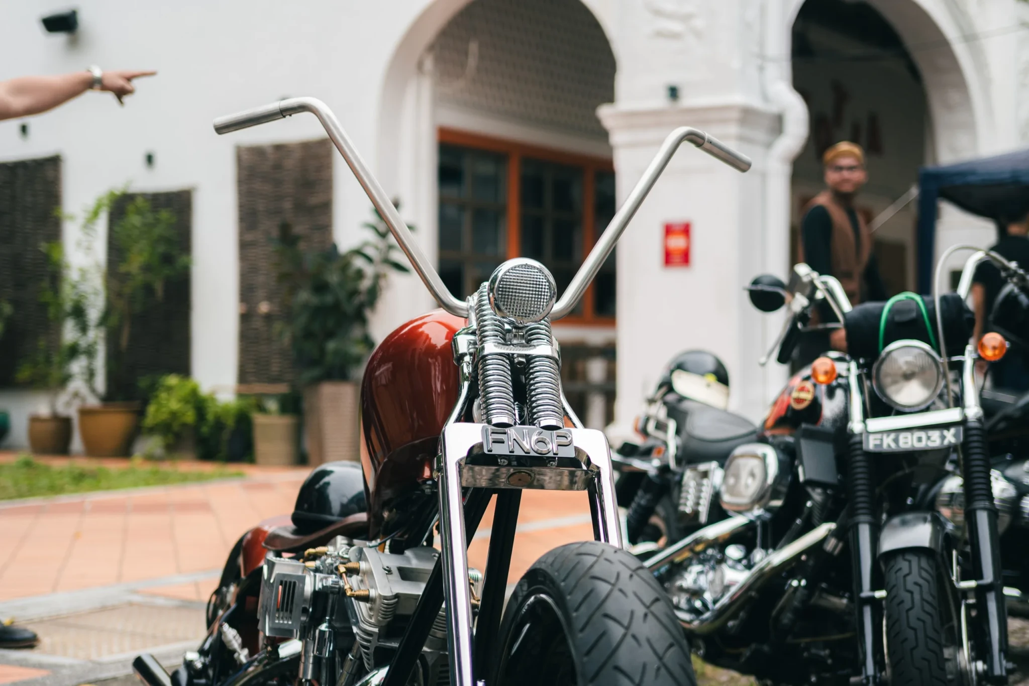 Custom motorcycle with burgundy tank and high-rise handlebars displayed among other bikes at outdoor festival