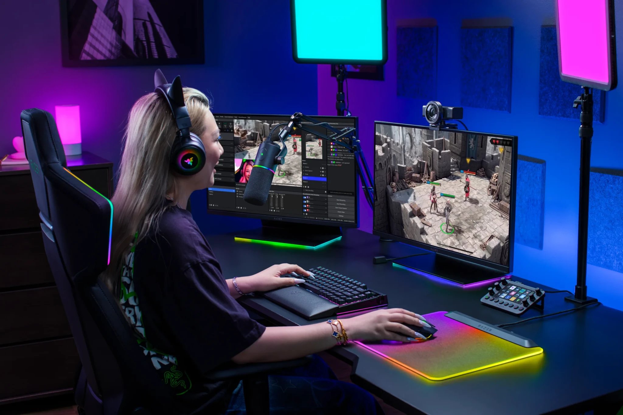 A creator wearing headphones at an RGB-lit gaming setup with the Razer Kiyo V2 Pro mounted above the right monitor