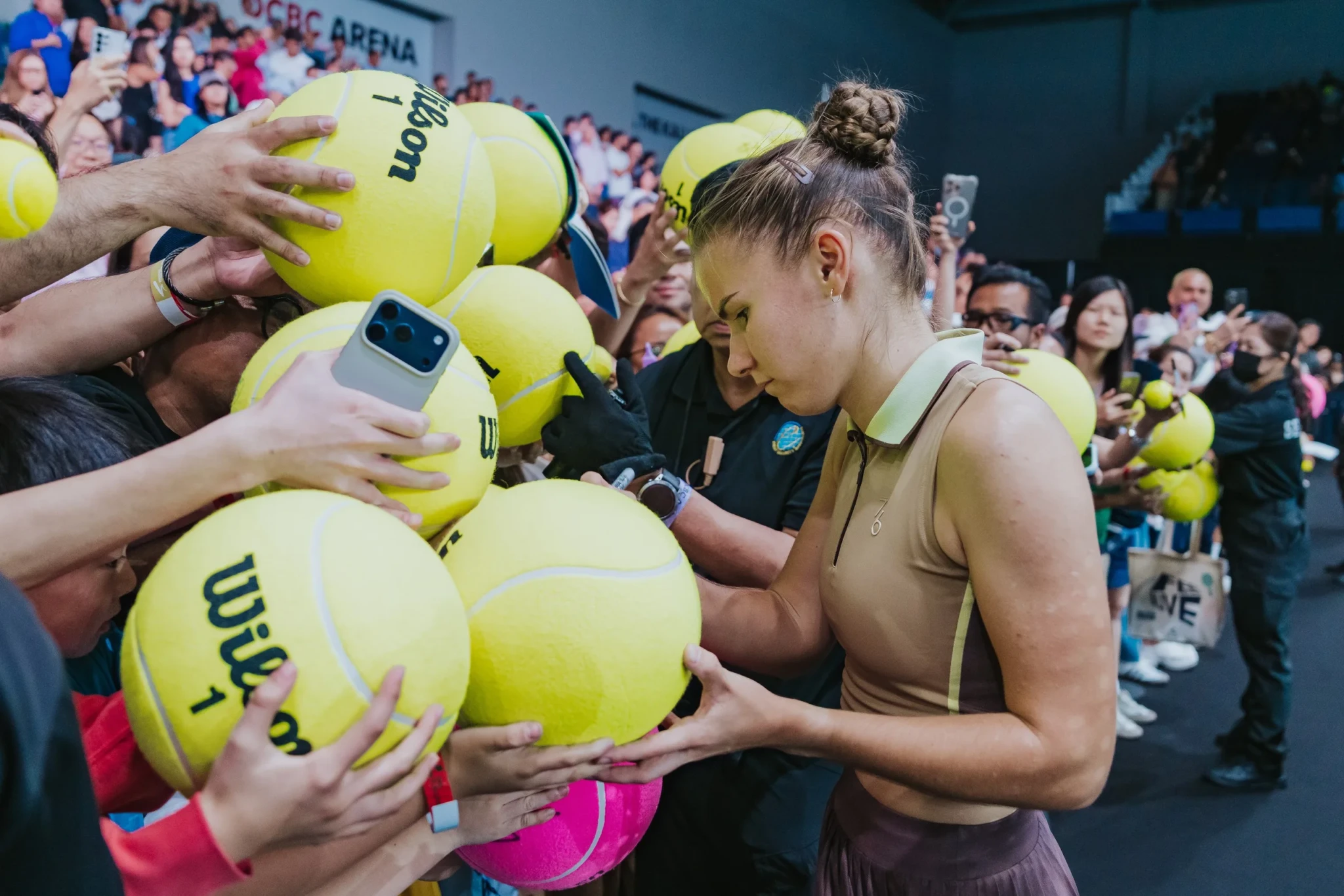 Tennis player signing yellow Wilson tennis balls for spectators at an indoor arena