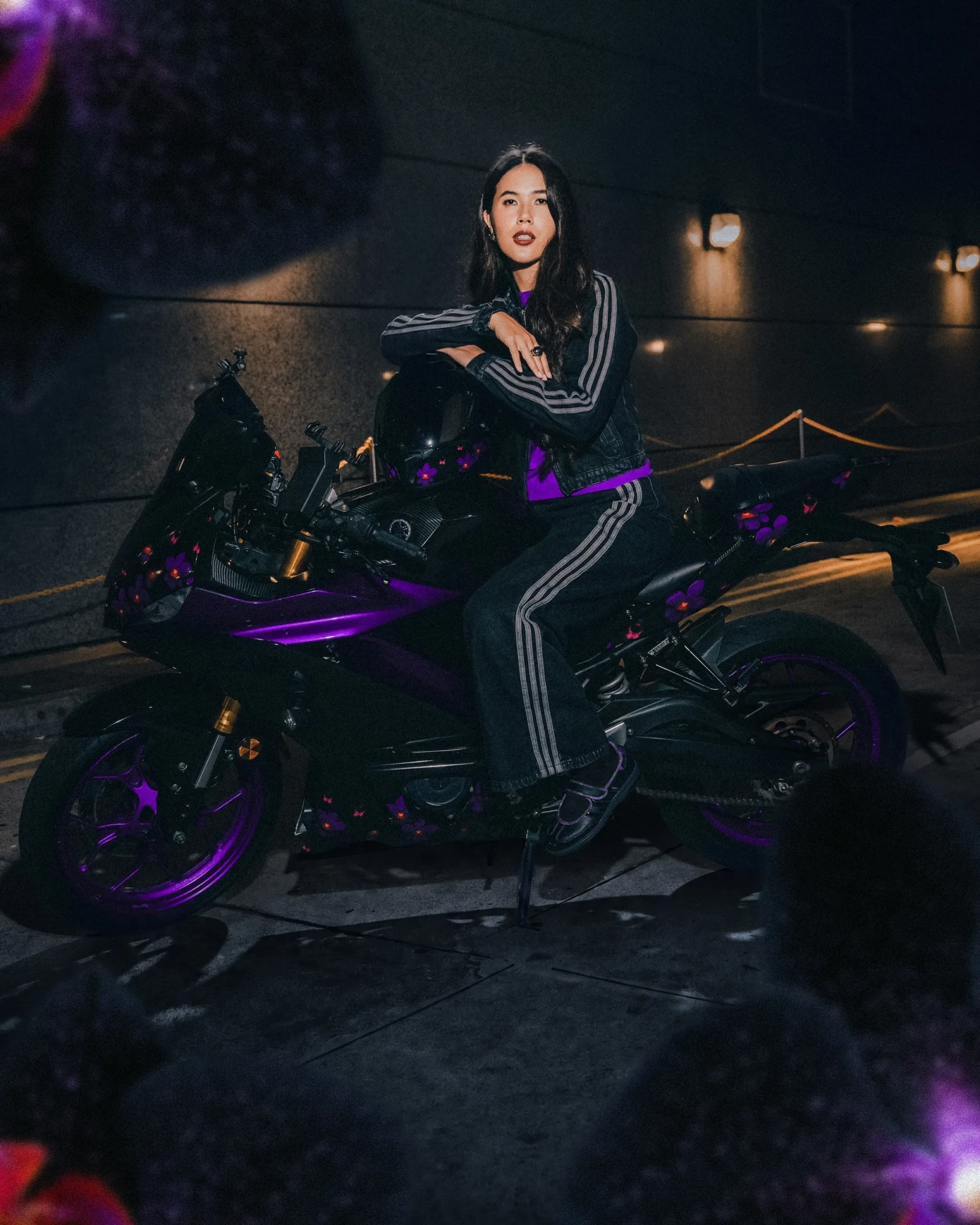 A model in an adidas Originals striped track jacket on a purple-lit motorcycle for the Black Orchid campaign