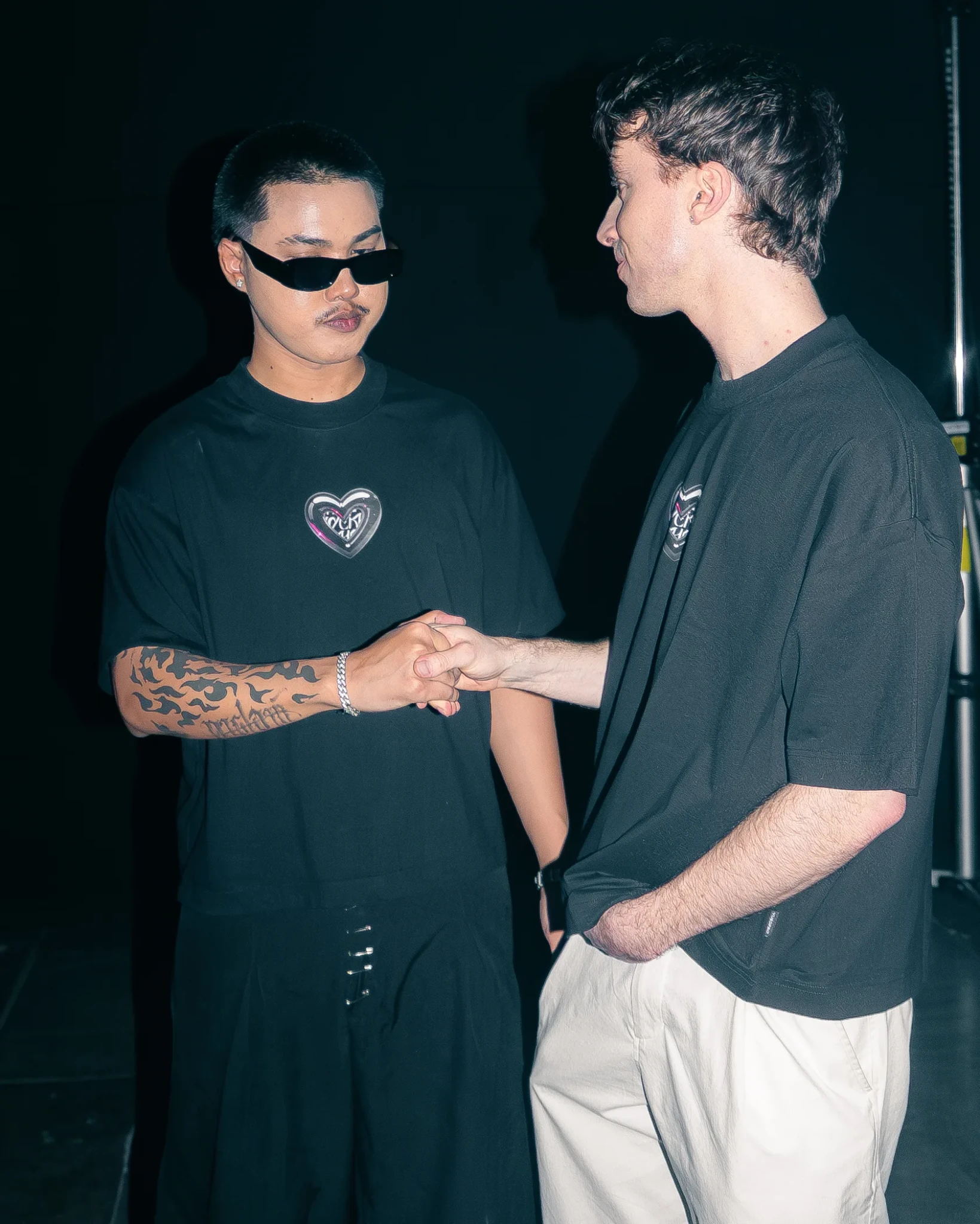 Two men in black t-shirts shaking hands against a dark background