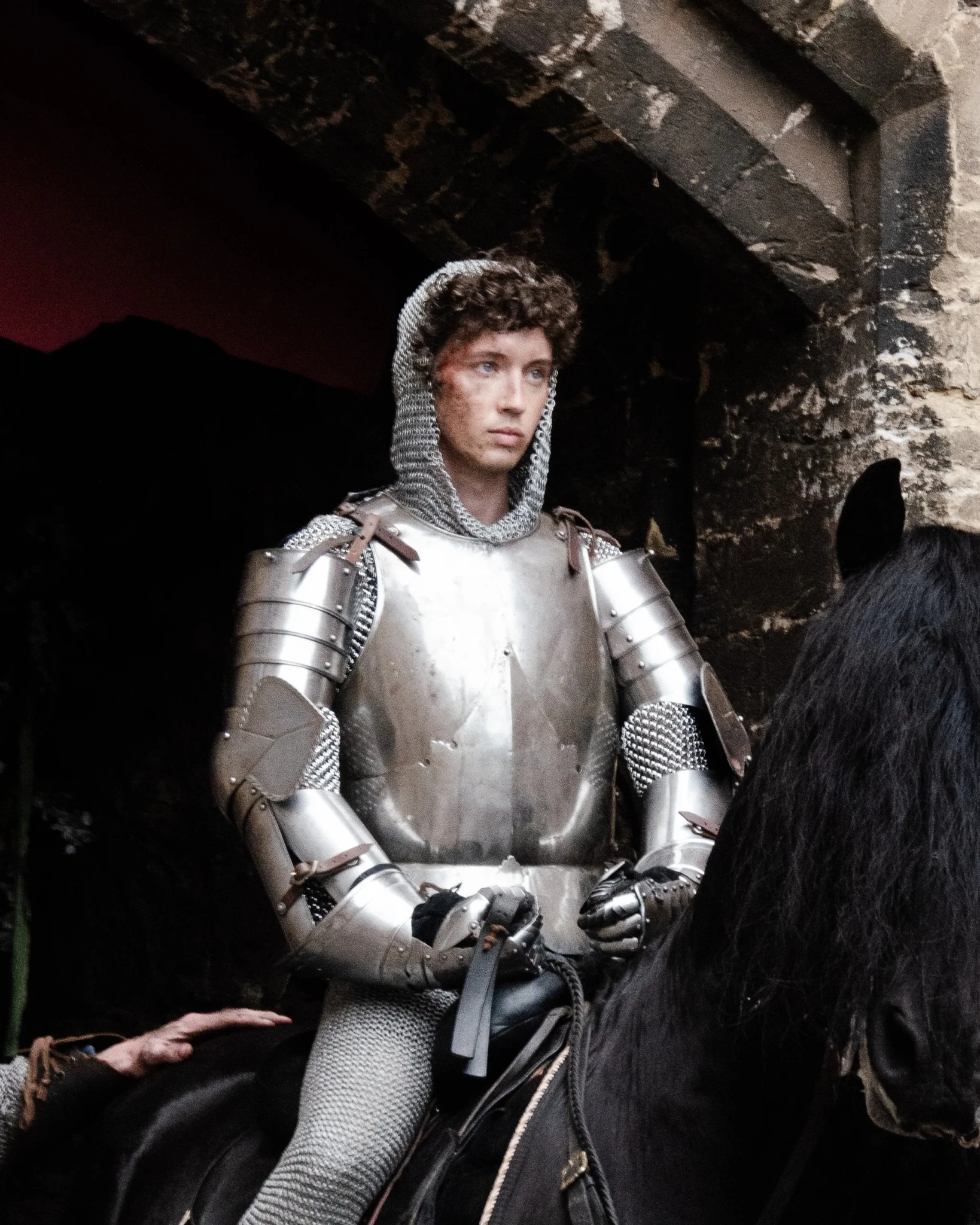 A knight in polished silver armour stands against a dark stone backdrop