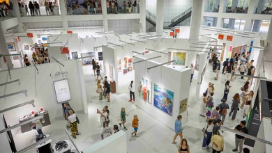 Visitors walking between exhibitor booths hung with paintings at Art & Bali 2026