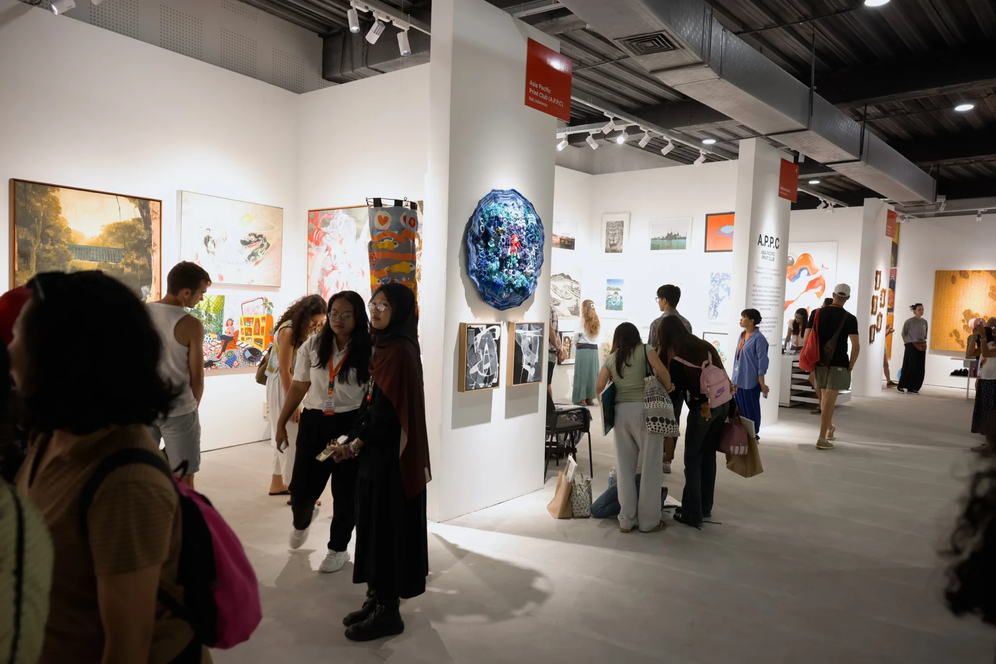 Visitors walk through a modern gallery space examining artworks including paintings and a blue sculptural installation.