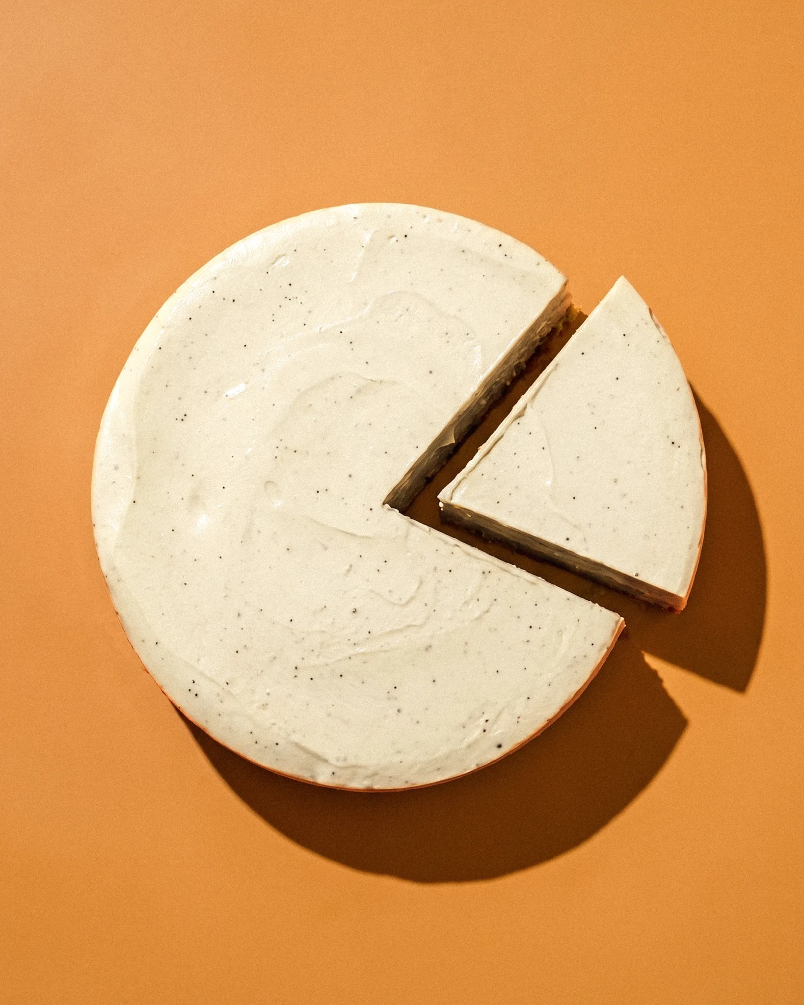 The Latte Cheesecake from Baristart Coffee and Queic by Olivia, shown whole with one slice cut out against an orange backdrop