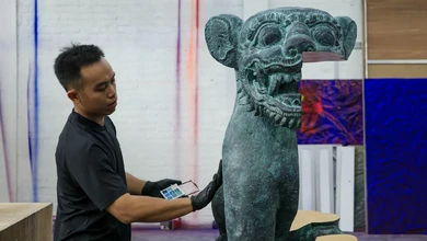 Jemana Murti holding a 3D scanner beside a traditional Balinese stone sculpture in his studio