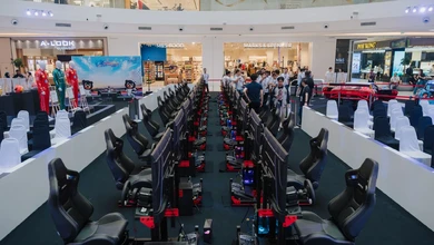 Racing simulators line a mall display, with spectators and rows of chairs.
