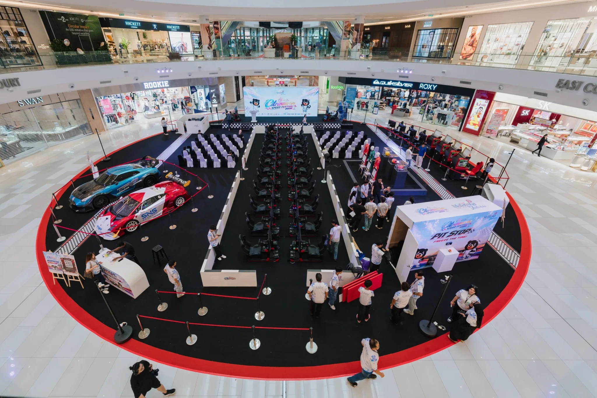 Racing simulator stations and two race cars in a shopping mall atrium