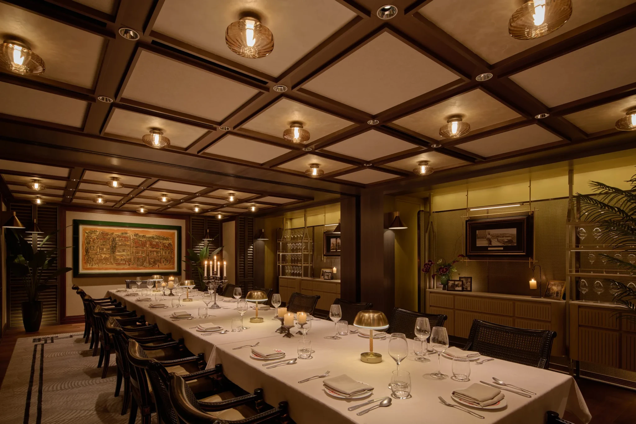 Formal dining table with white linens, place settings, glassware, and brass table lamps in an upscale private dining room with dark wood beams